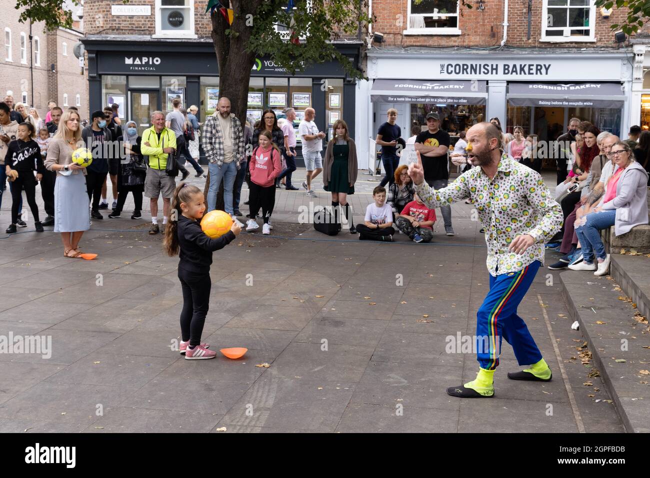 Street Performer UK - ein Street Entertainer in York, der mit einem Kind vor einer Menschenmenge auftrat, Kings Square, York City Centre, York Yorkshire UK Stockfoto