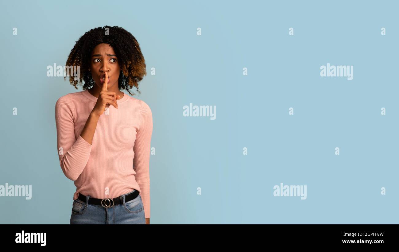 Ruhe Bewahren. Sorge Schwarze Frau Hält Den Finger In Der Nähe Der Lippen Und Schaut Weg Stockfoto