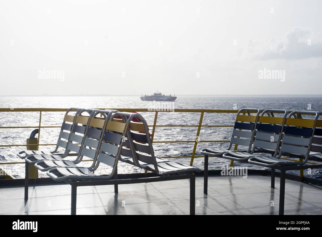 Offenes Deck einer Fähre mit leeren Stühlen, die im Karibischen Ozean in Mexiko segelt. Am Horizont ein Handelsschiff Stockfoto