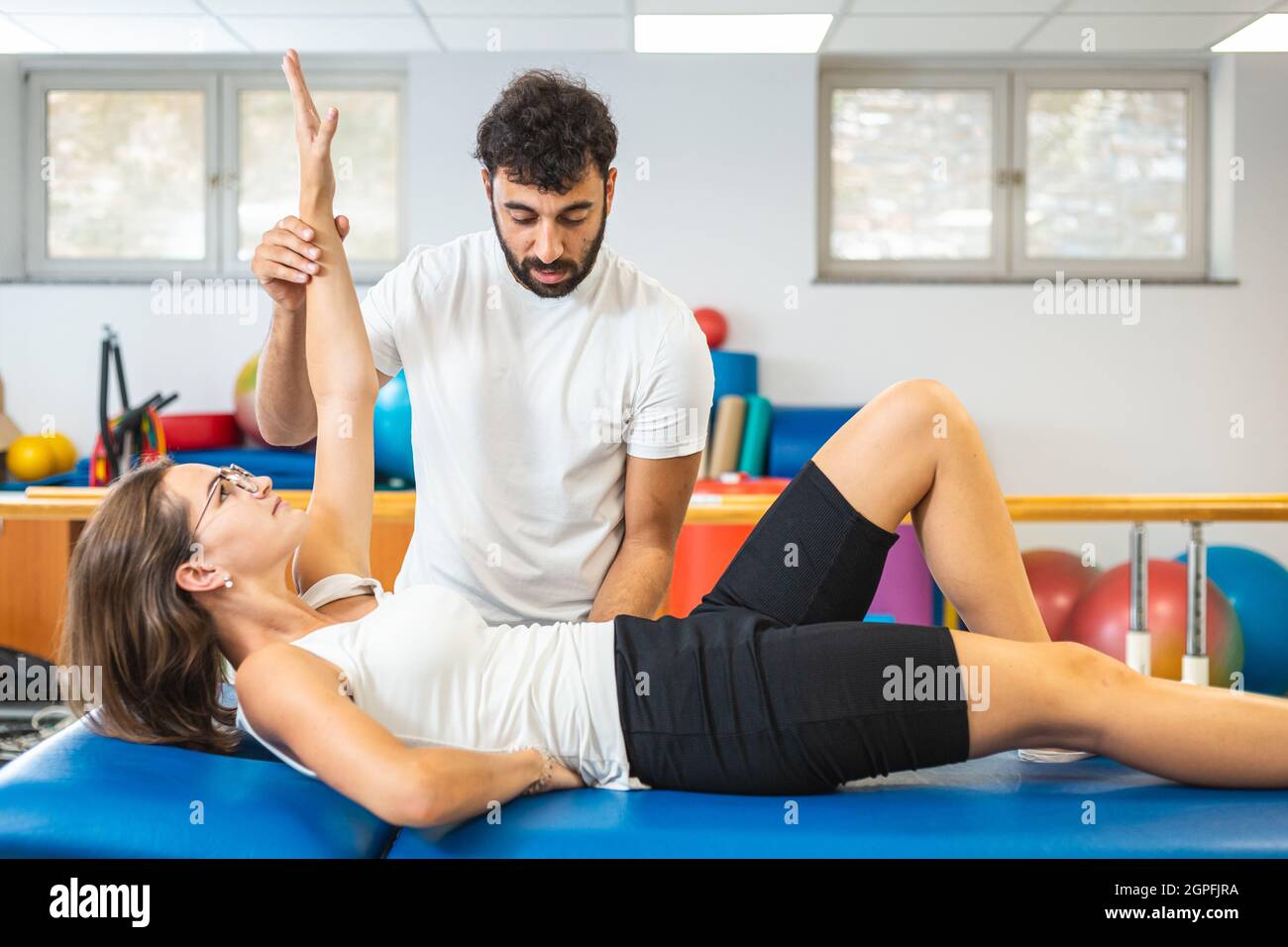 Frau, die auf dem Rücken liegt und Oberkörperübungen mit Hilfe eines männlichen Physiotherapeuten macht. Stockfoto