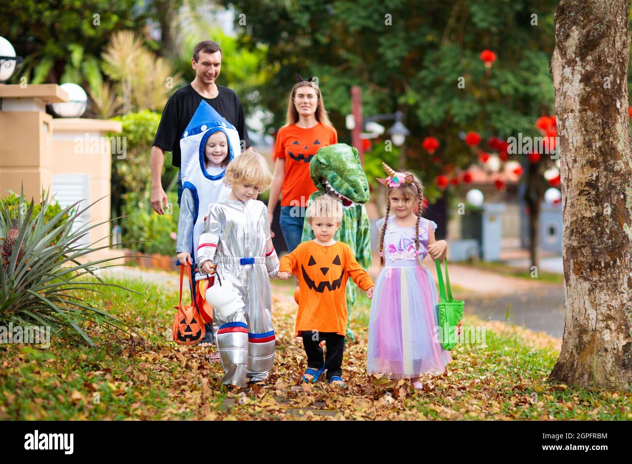 Kind in Halloween-Kostüm. Asiatische und kaukasische Kinder und Eltern mit gemischten Rassen tricksen oder gönnen sich auf der Straße. Kleiner Junge und Mädchen mit Kürbislaterne und Dose Stockfoto