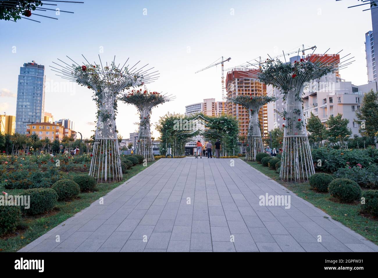 Maltepe, Istanbul, Türkei - 07.22.2021: Baumstraße des öffentlichen Parks Cumhuriyet (Republik) und Menschen, die am Abend beim Skateboarden herumsitzen Stockfoto