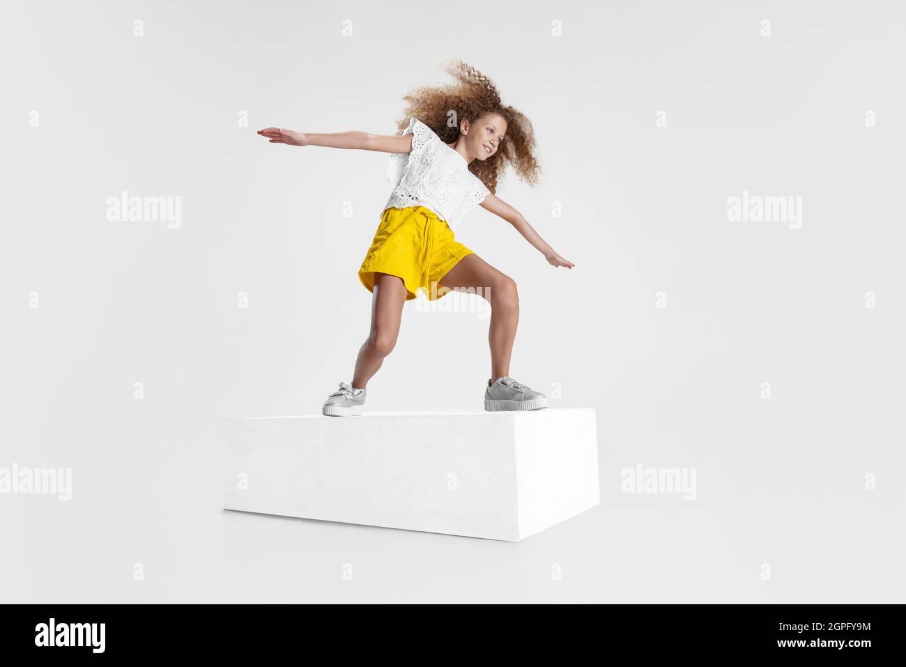 In voller Länge Porträt eines lächelnden Mädchen in legerer Kleidung auf großen Box isoliert auf weißem Studio Hintergrund stehen. Happy Childhood Konzept. Stockfoto