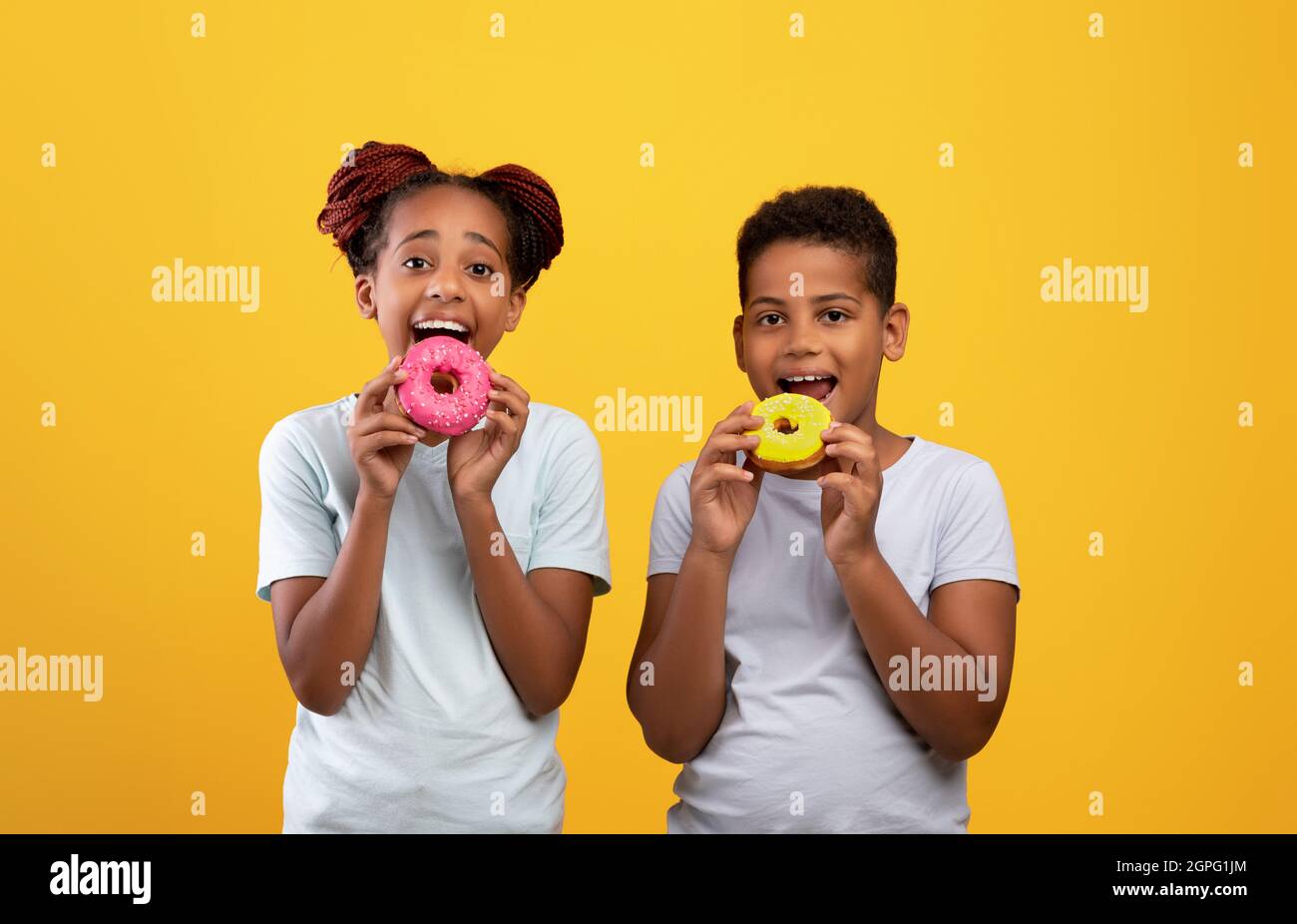Glücklich schwarzen Jungen und Mädchen essen köstliche Donuts Stockfoto