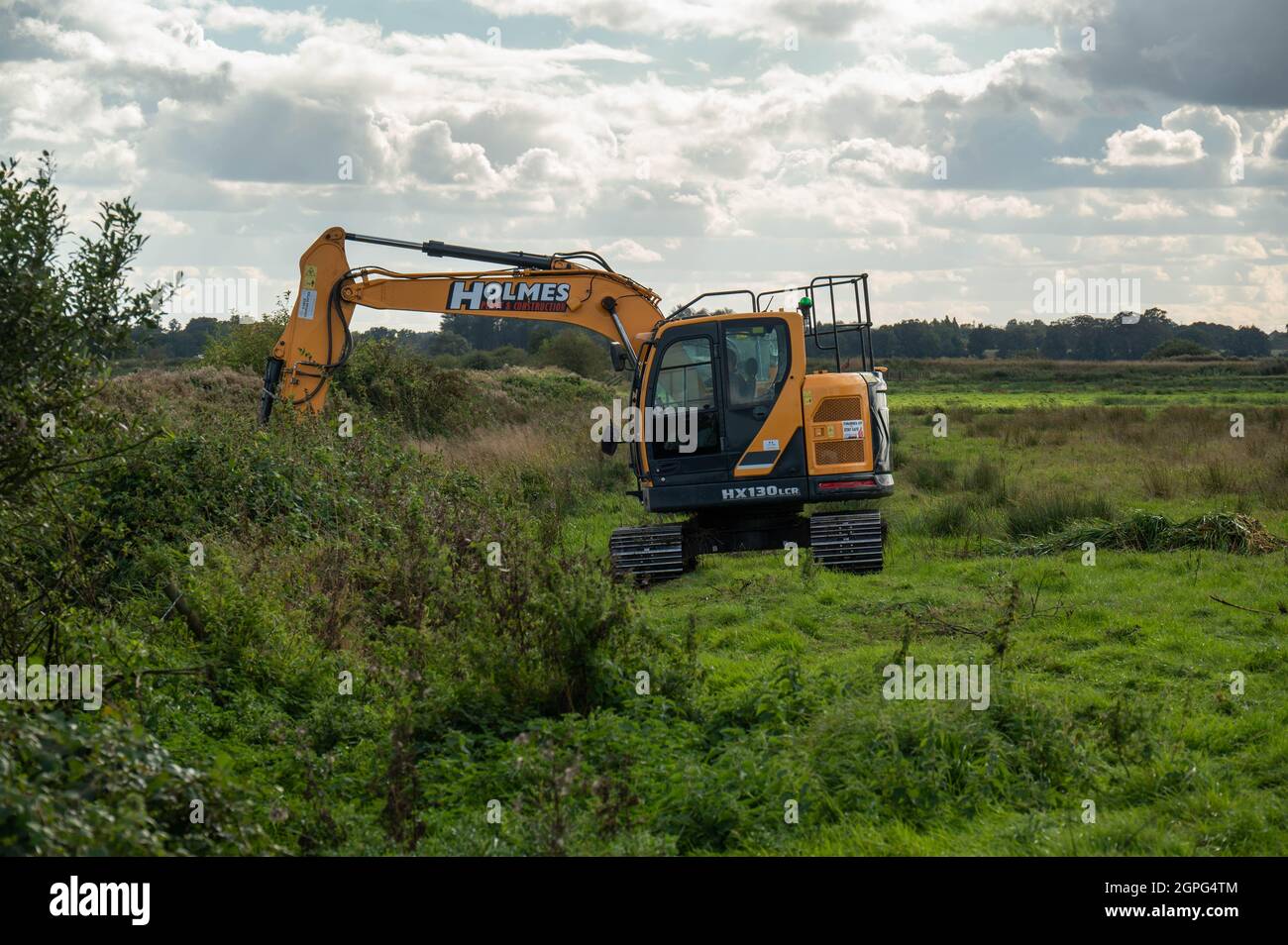 Ein Bagger, der Abflussgräben auf niedrig gelegenen grasenden Sumpfschümpfen auf den Norfolk Broads bei Buckenham Marshes beibehält Stockfoto