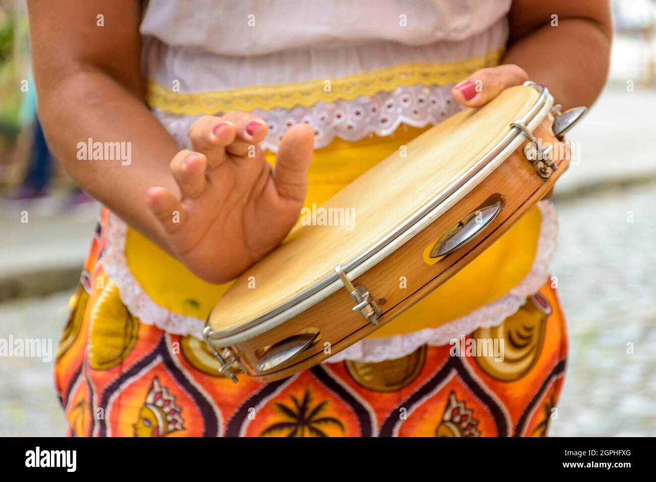 Junge Frau in farbenfrohen Kleidern spielt Tamburin während einer Samba-Aufführung in Salvador, Bahia. Stockfoto