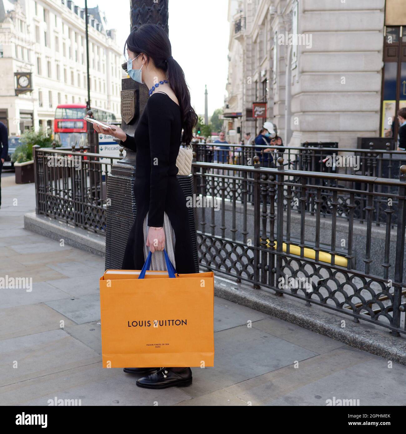 London, Greater London, England, September 21 2021: Eine elegante asiatische Dame in einem schwarzen Outfit prüft ihr Telefon, während sie eine Louis Vuitton Einkaufstasche trägt Stockfoto