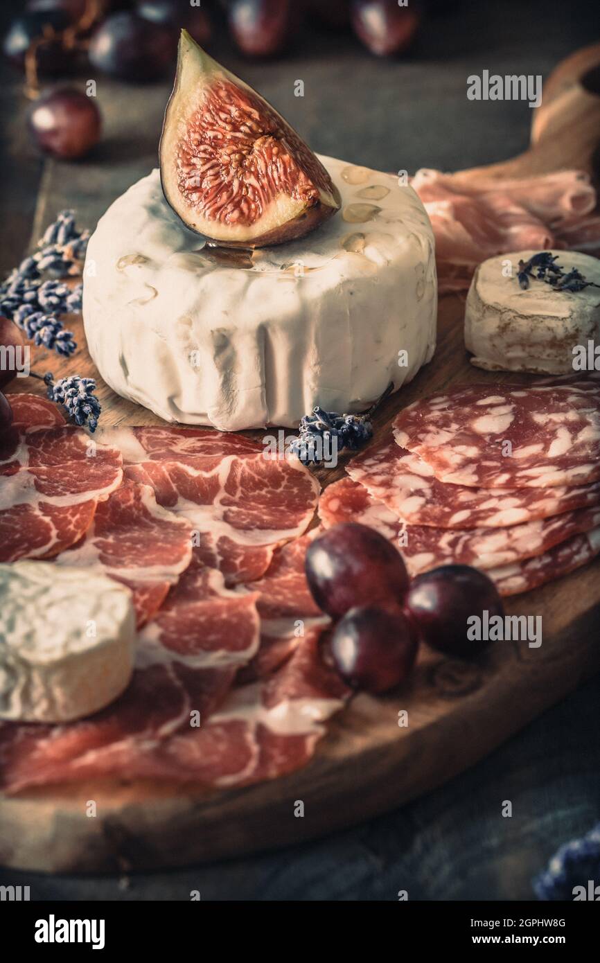 Verschiedene geräucherte Wurst Spezialitäten und ein weicher Käse auf einem Holzbrett, mit Feigen und Trauben geschmückt, konzentrieren sich auf den Käse, vertikal Stockfoto