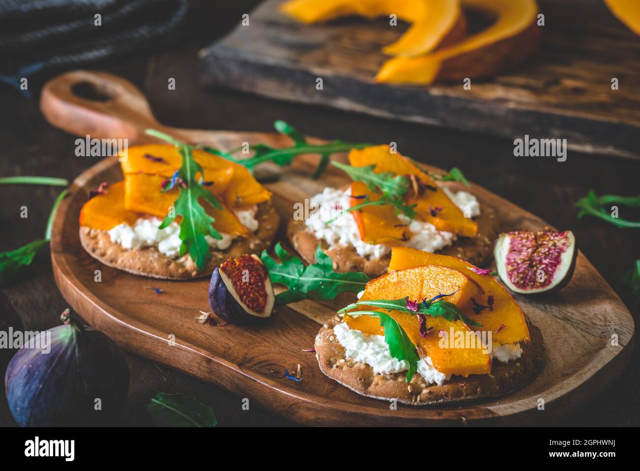 Runde Knäckebrot-Scheiben mit körniger Frischkäse, geröstetem Kürbis und Rucola auf Holzboden Stockfoto