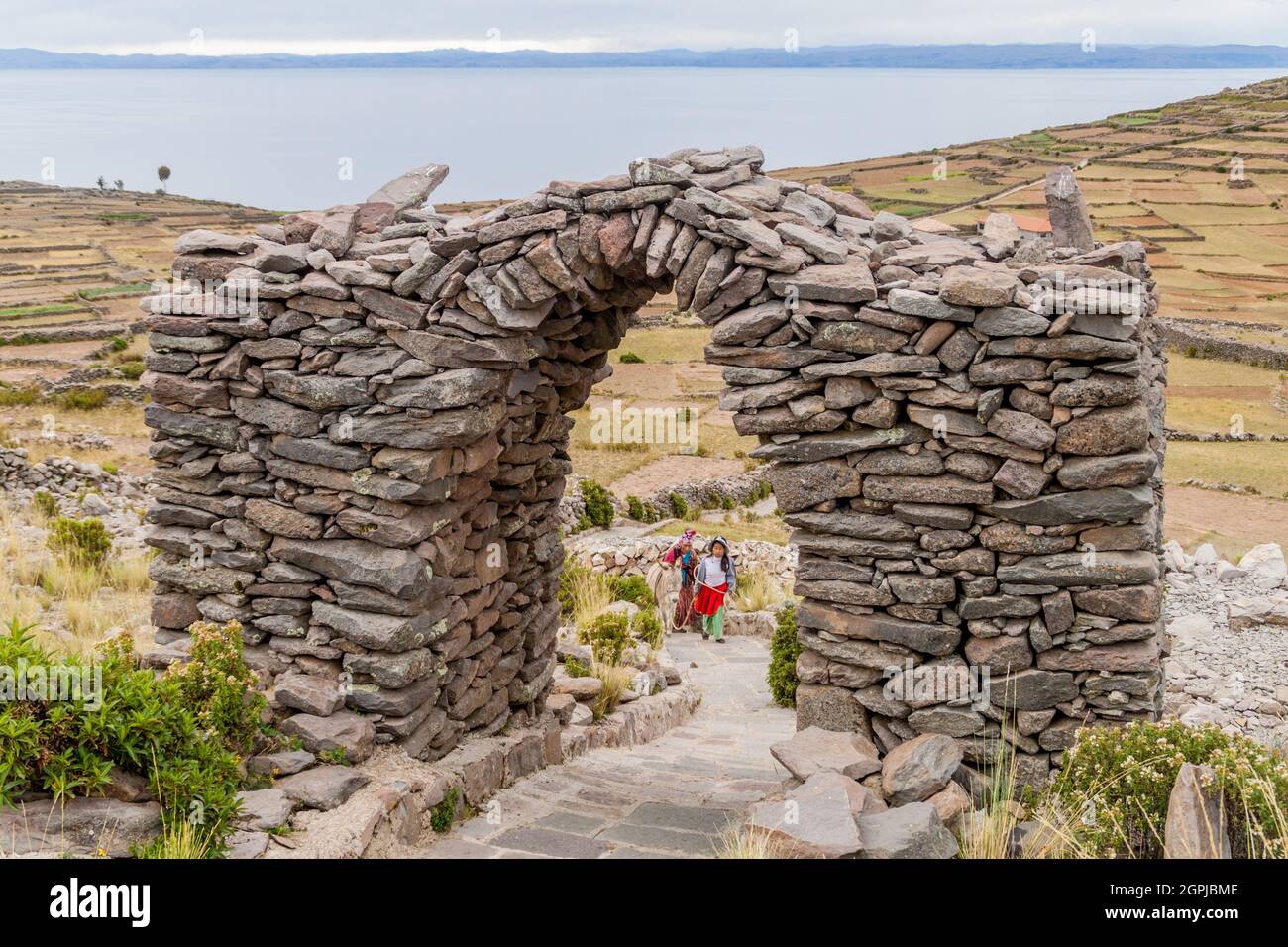 AMANTANI, PERU - 15. MAI 2015: Die Einheimischen gehen auf einem Pfad durch einen Steinbogen auf dem Pachatata-Hügel auf der Insel Amantani im Titicaca-See, Peru Stockfoto