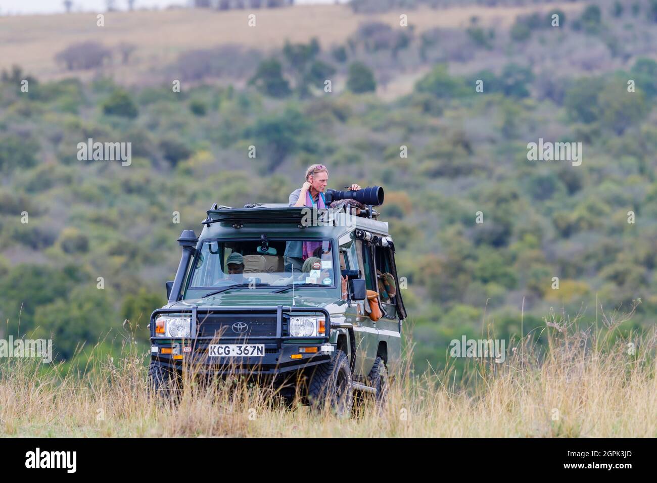 Safari Touristen stehen Ihre lange Teleobjektive auf die Tierwelt aus einer typischen offenen Jeep Safari in die Masai Mara, Kenia zu trainieren Stockfoto