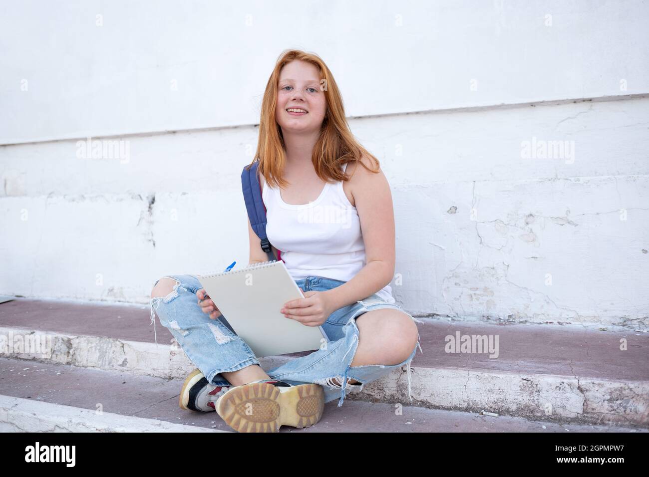 Das Teenager-Mädchen zeichnet das Skizzenbuch, während es auf den Stufen sitzt. Stockfoto