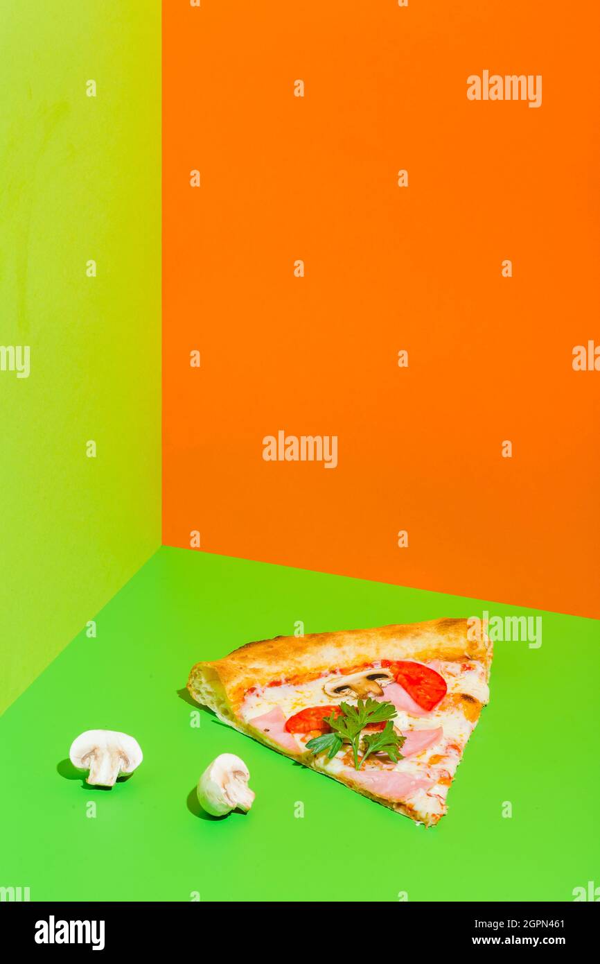 Pizza mit Schinken und Pilzen auf papiergrünem und orangefarbenem Hintergrund Stockfoto