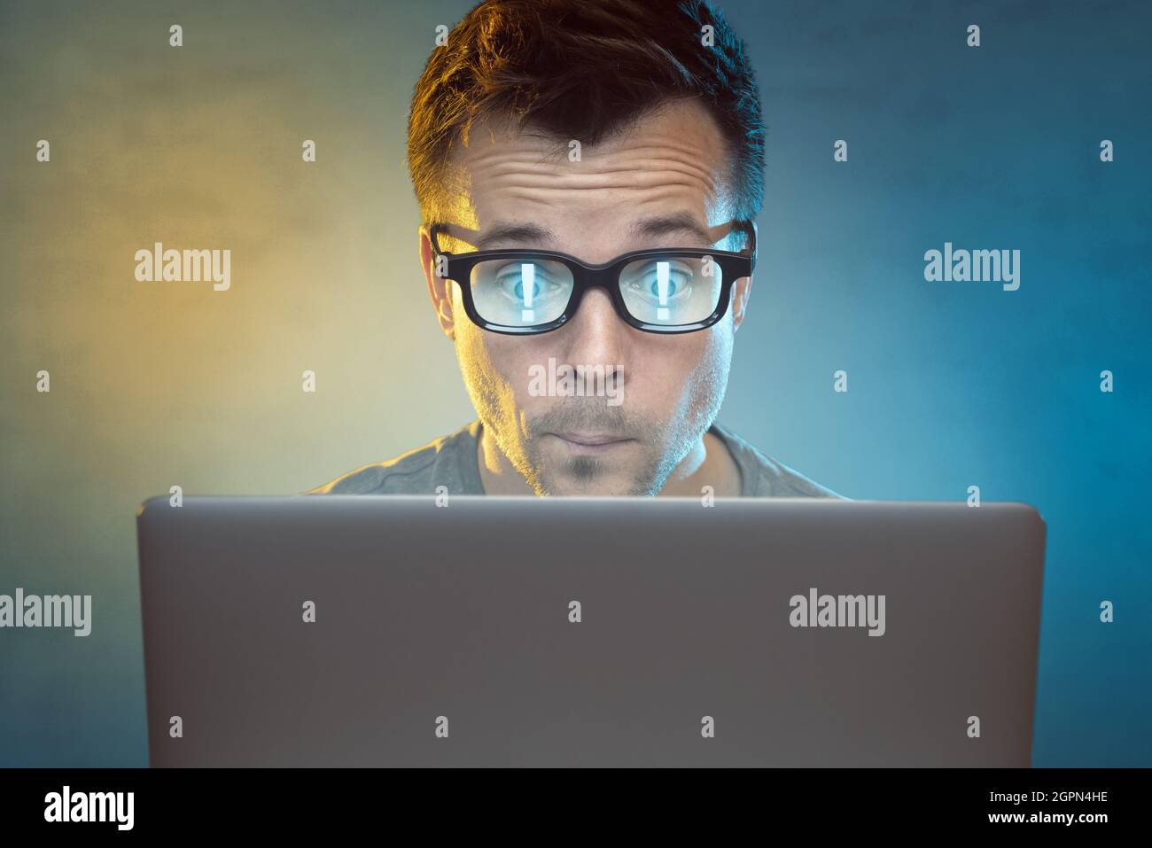 Mann vor einem Computer mit Ausrufezeichen, die sich in seiner Brille spiegeln Stockfoto