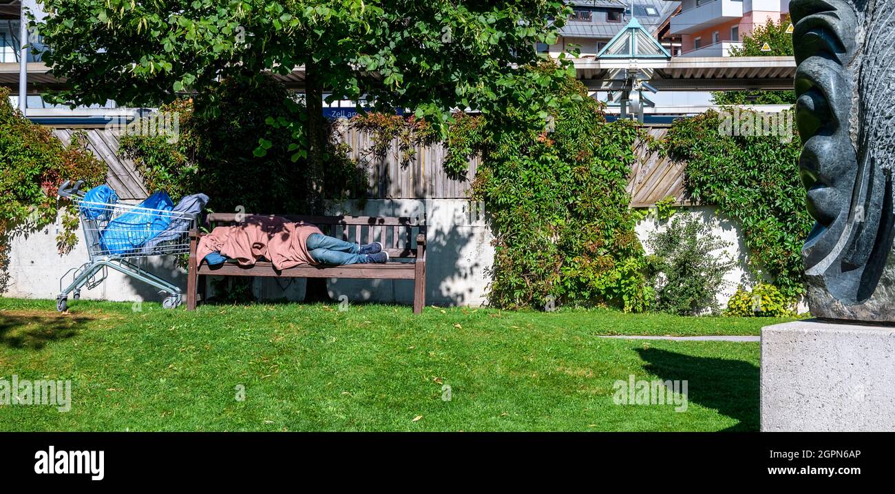 Obdachlose, die bei Sonnenschein in der Nähe eines steinernen Kunstwerks in einem Park in Zell am See, Österreich, schlafen Stockfoto