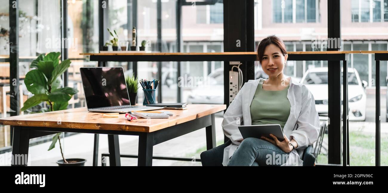 Porträt einer attraktiven asiatischen Geschäftsfrau, die in ihrem Büro an einem Laptop und einem digitalen Tablet für einen Marketingplan arbeitet Stockfoto