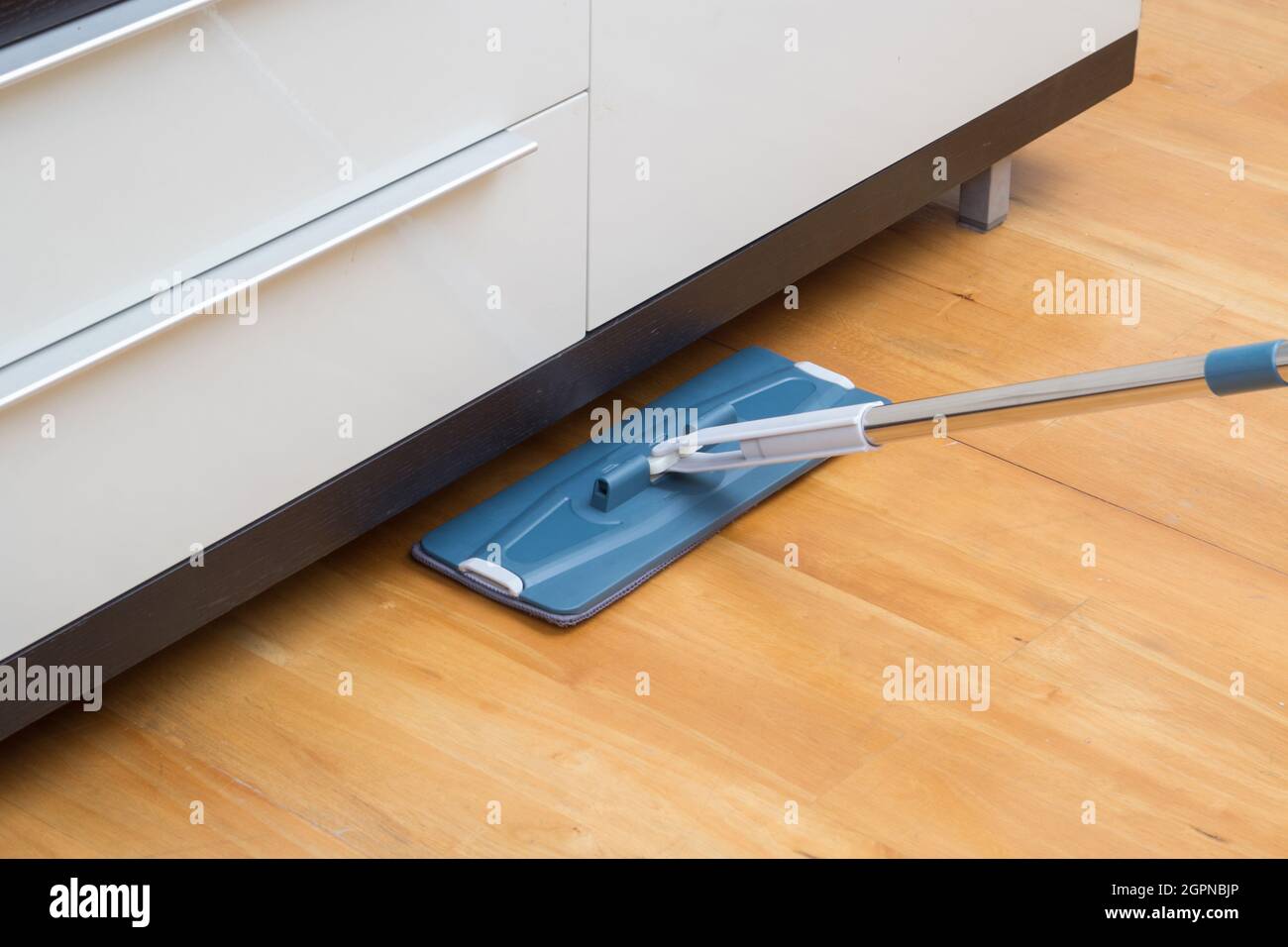 Haushälterin wischen Holzboden mit Mopp unter dem Schrank Stockfoto