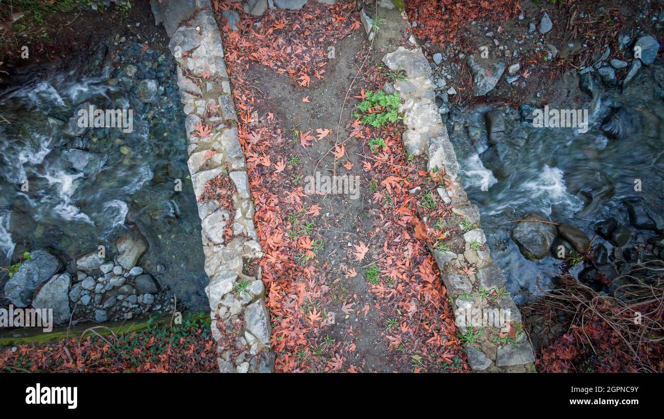 Mittelalterliche Steinbrücke über Waldbach im Herbst mit gefallenen Blättern bedeckt, Luftaufnahme direkt darüber Stockfoto