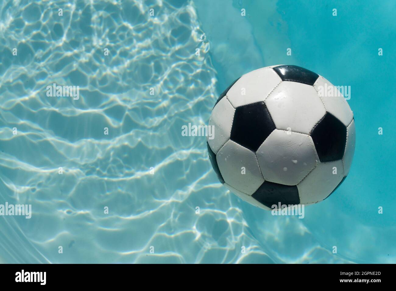 Schwarz-weißer Fußball, schwimmend in einem blau-klaren Schwimmbad. Sommer Sport Hintergrund Stockfoto