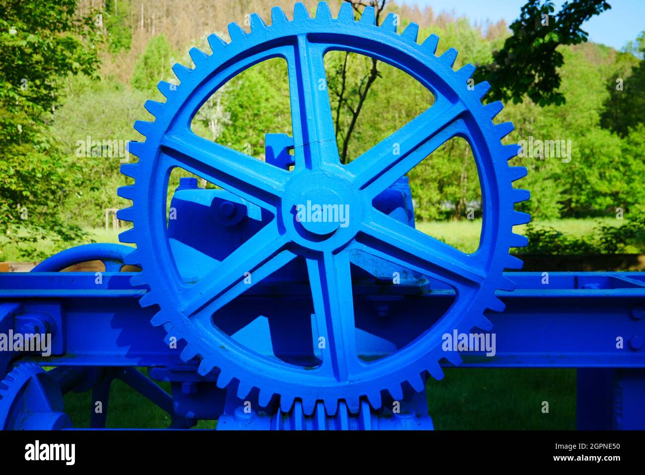 Großes blau lackiertes Metallgetriebe als Antriebsteil für einen Wasserdamm in einem Waldfluss Stockfoto