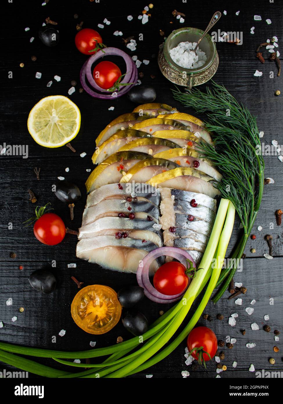 In Scheiben geschnittener Fisch, gesalzener Hering, geräucherter Makrele mit Kirschtomaten, grünen Zwiebeln, Dill, Zitrone und Gewürzen Stockfoto