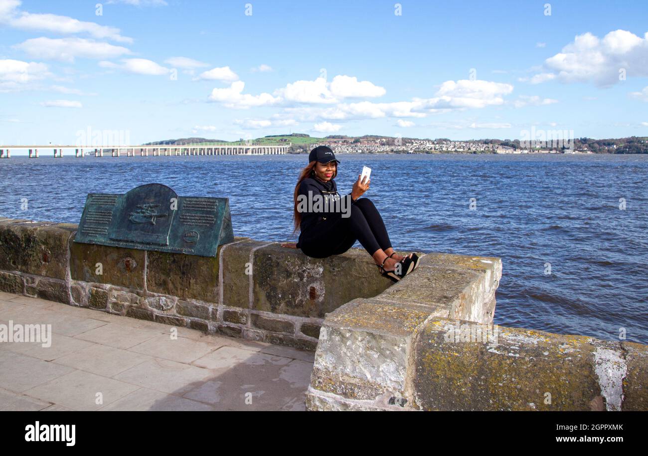 Eine glückliche Afrikanerin ist unterwegs und genießt den warmen Sonnenschein, während sie auf dem Fluss Tay in Dundee, Schottland, für Fotos posiert Stockfoto
