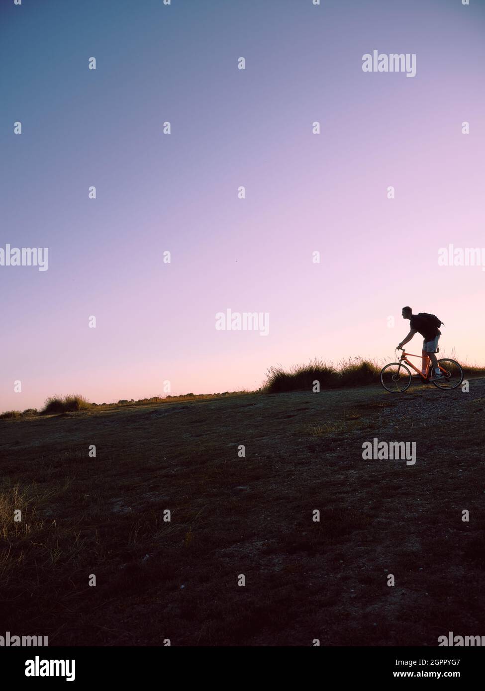 Ein einmotoriger Mountainbike-Radfahrer hinterleuchtet in den späten Abend Sommer grasbewachsenen Landschaft und Himmel - Offroad-Radfahren - Copy Space - einmotorige Radler Landschaft Stockfoto