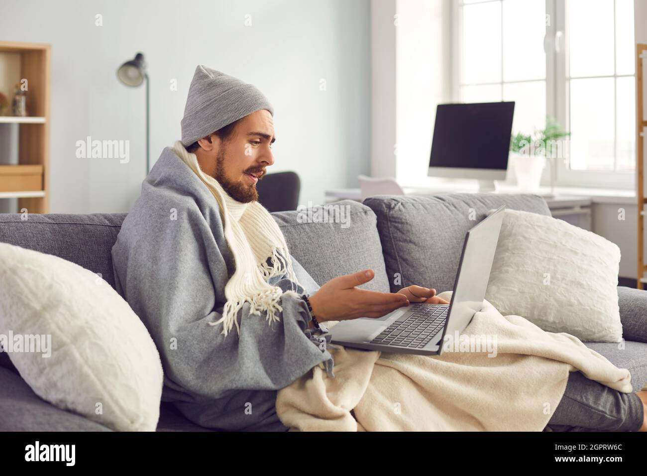 Kranker Mann in warmer Kleidung, der dem Arzt online Krankheitssymptome erzählt Stockfoto