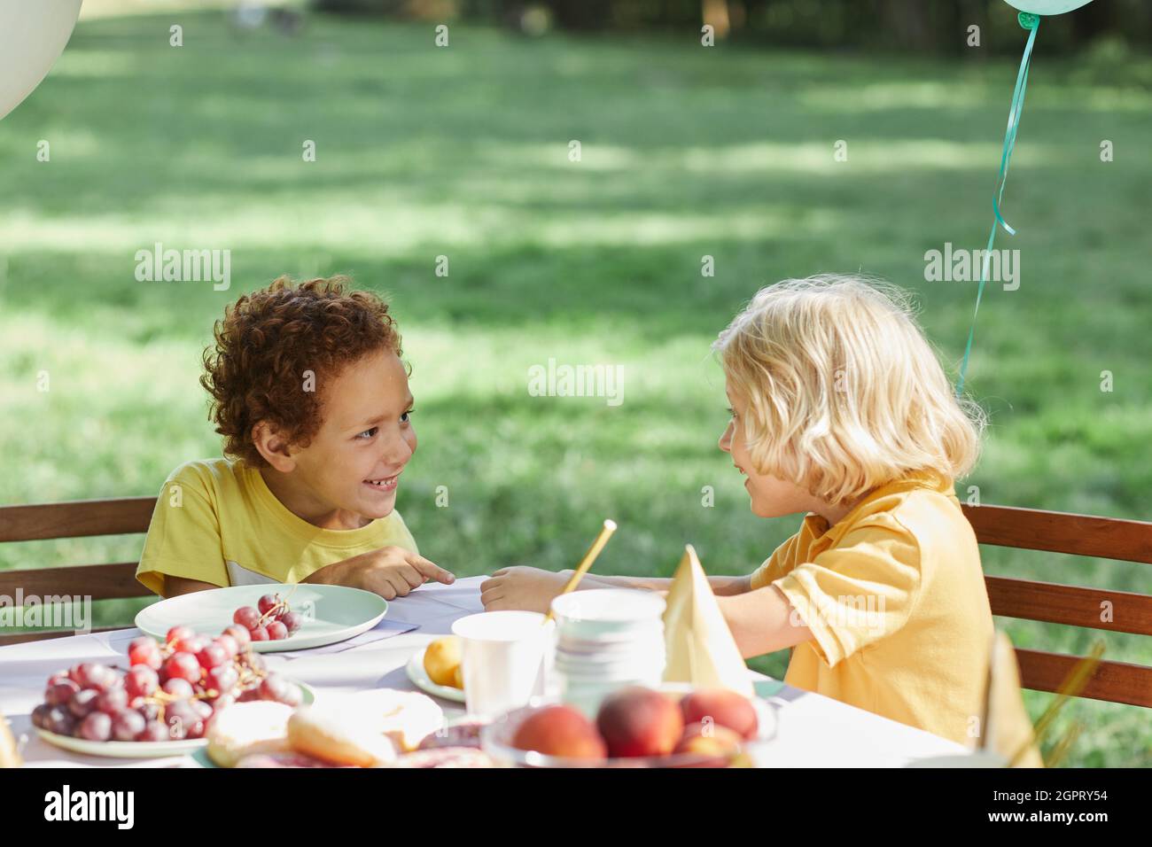 Zwei kleine Kinder am Picknicktisch im Freien mit Luftballons für Geburtstagsfeier im Sommer geschmückt, kopieren Platz Stockfoto