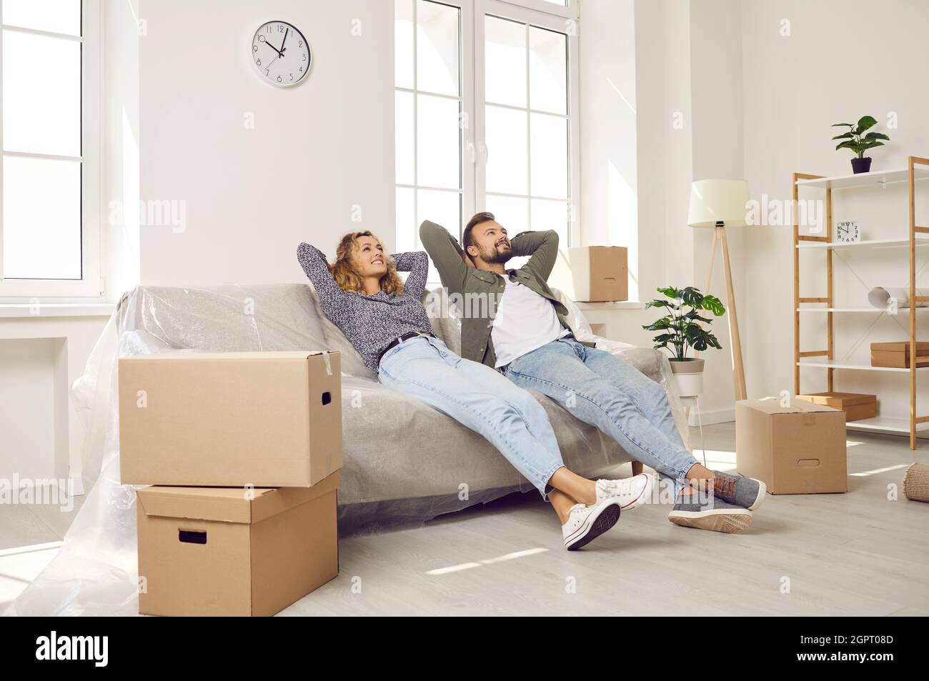 Glückliches Paar, das eine Pause macht und auf einer Couch sitzt, während es in ihrem neuen Haus umzieht Stockfoto