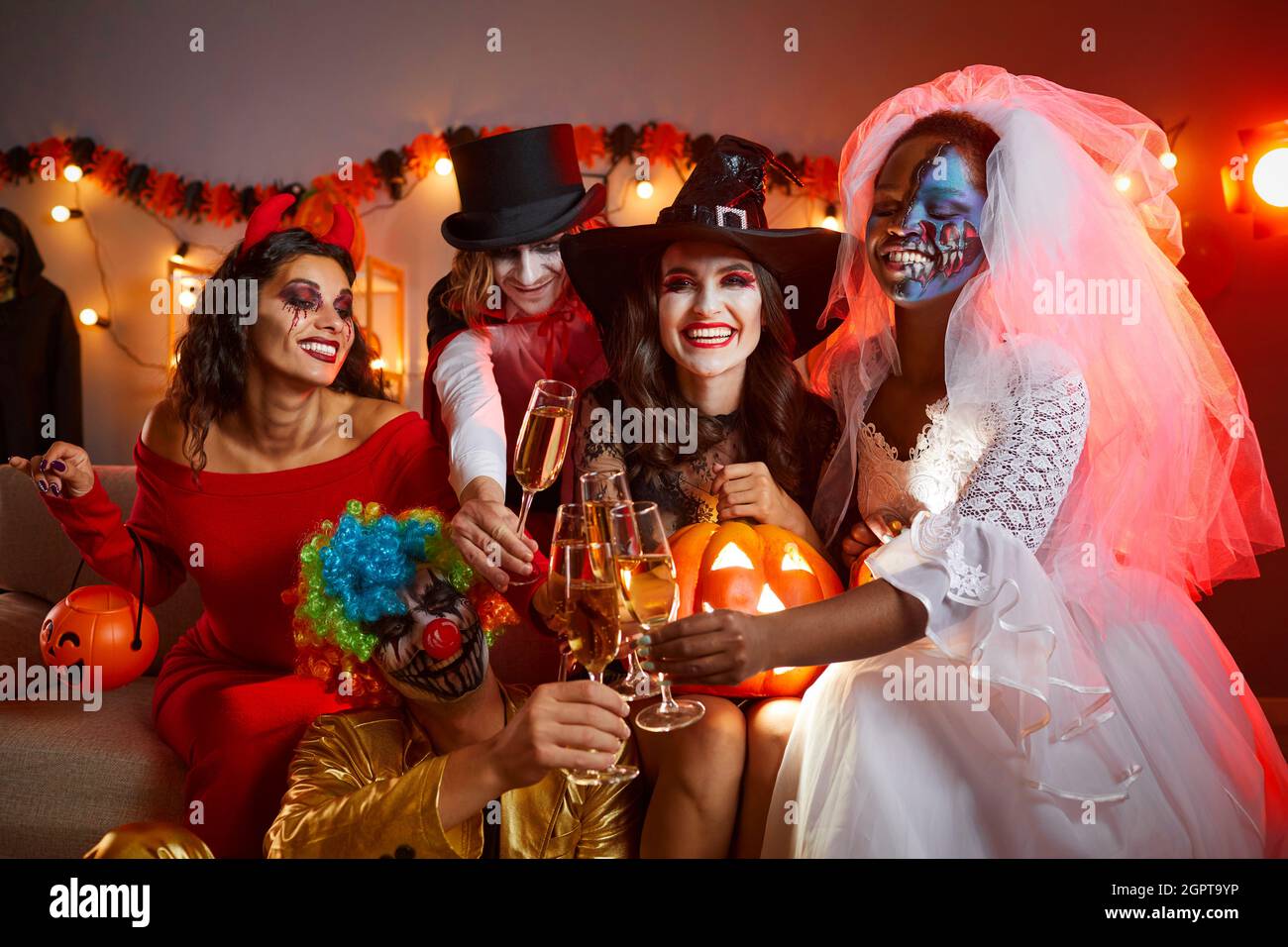 Eine bunte Gruppe von fröhlichen jungen Freunden, die auf einer Halloween-Party trinken und Spaß haben Stockfoto