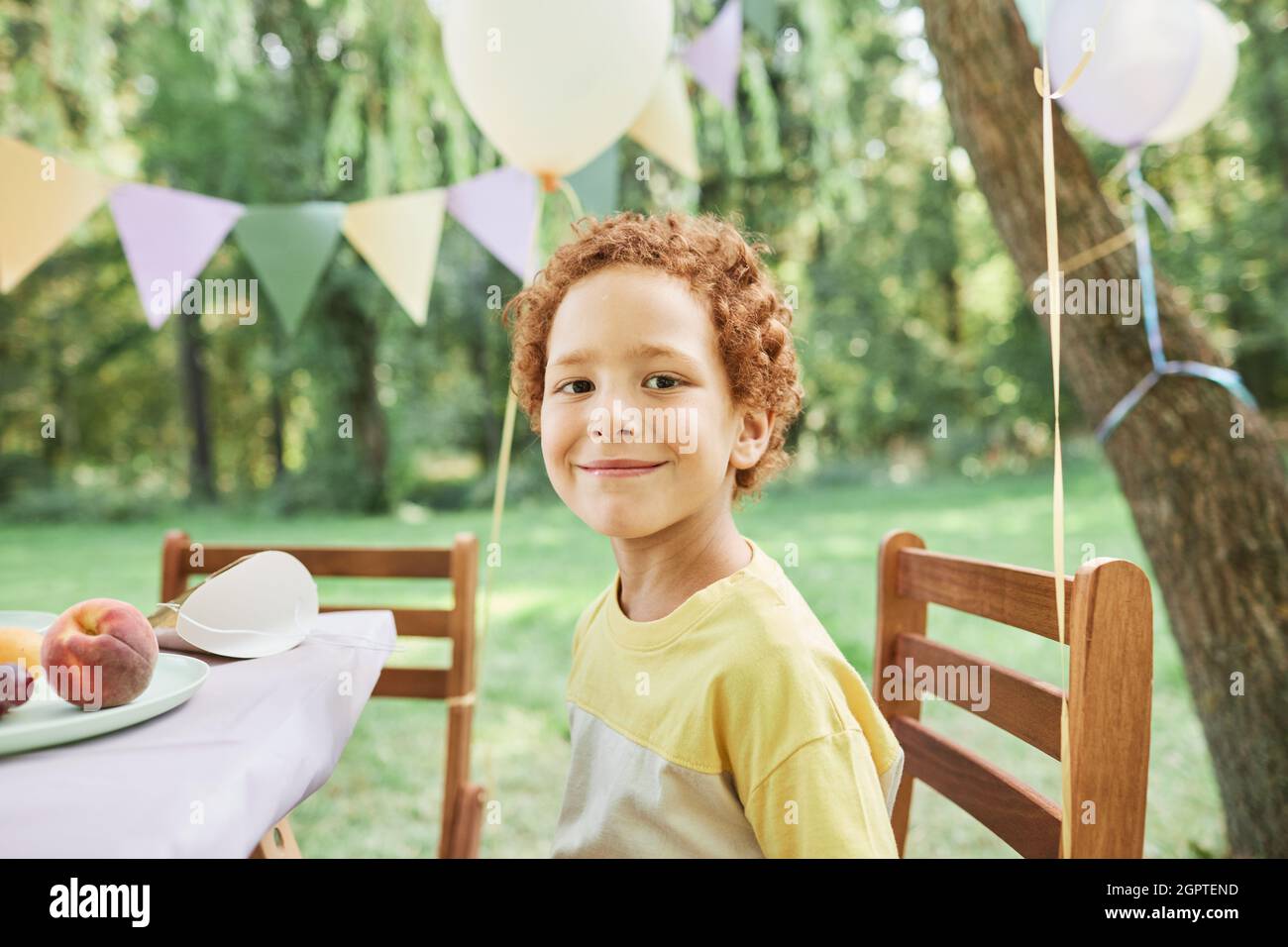 Porträt eines lächelnden Jungen, der im Sommer auf die Kamera am Picknicktisch im Freien schaut und die Geburtstagsfeier genießt Stockfoto