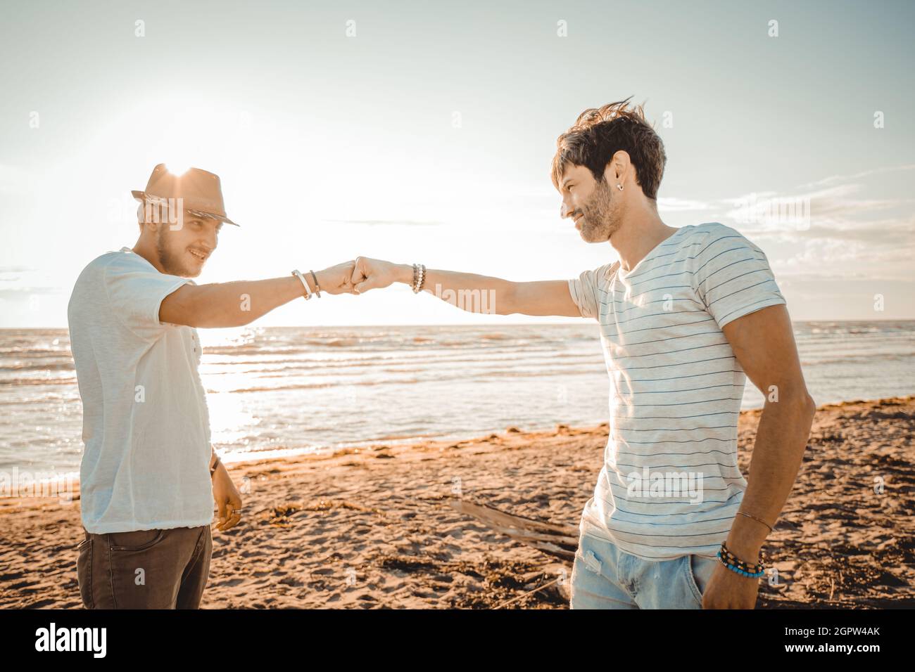 Zwei kaukasische lächelnde Jungs am Strand begrüßen sich gegenseitig mit einer Faust - treffen Konzept, zeigen Respekt und Freundschaft, die eine gute Beziehung haben Stockfoto