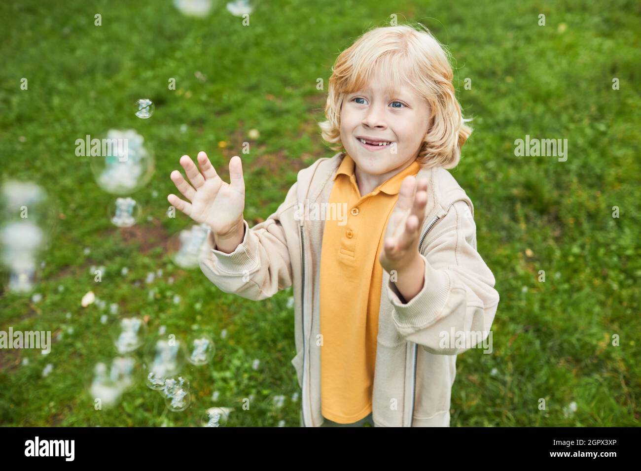 Porträt von niedlichen blonden Jungen spielen mit Blasen im Freien im Park und lächeln, kopieren Raum Stockfoto