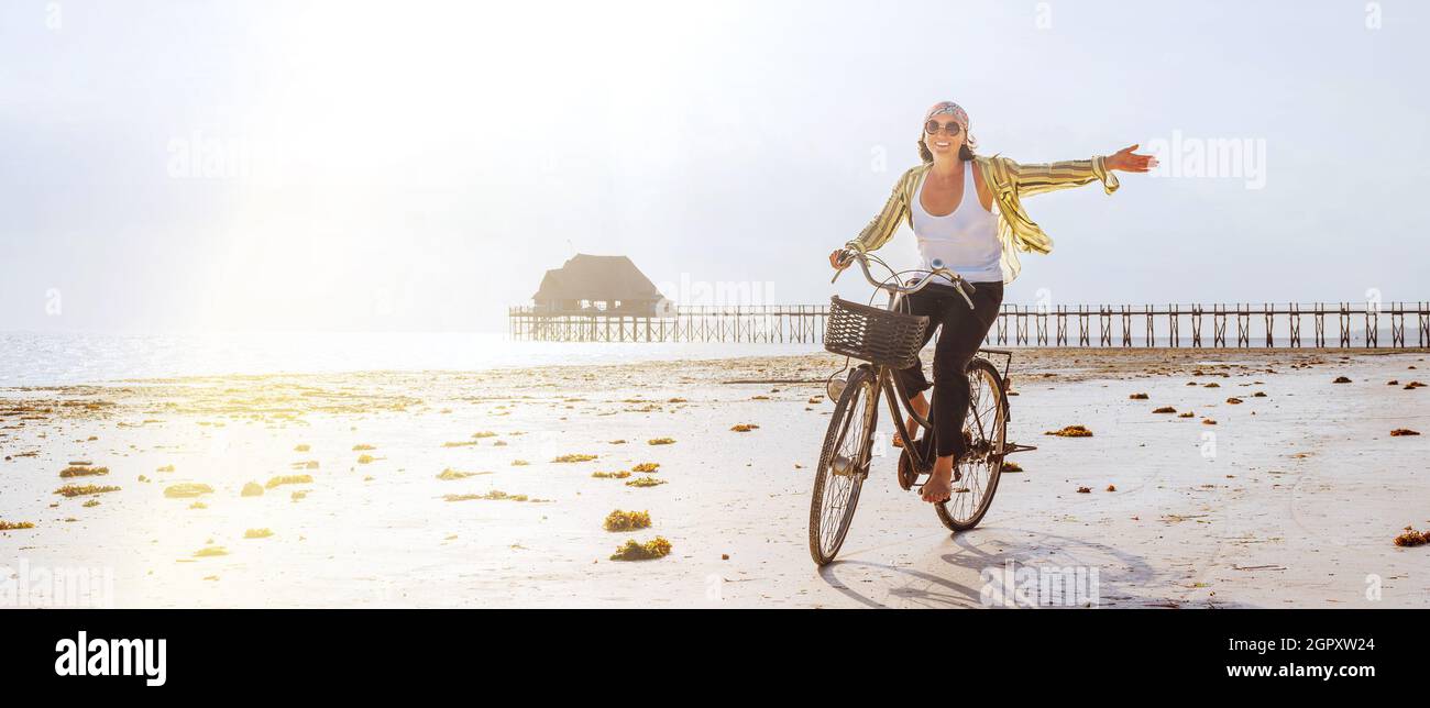 Junge weibliche gekleidete leichte Sommerkleidung freudig warf sie Hand Reiten alte Vintage-Fahrrad mit Vorderkorb auf dem Ebbe Ozean weißen Sand coa Stockfoto
