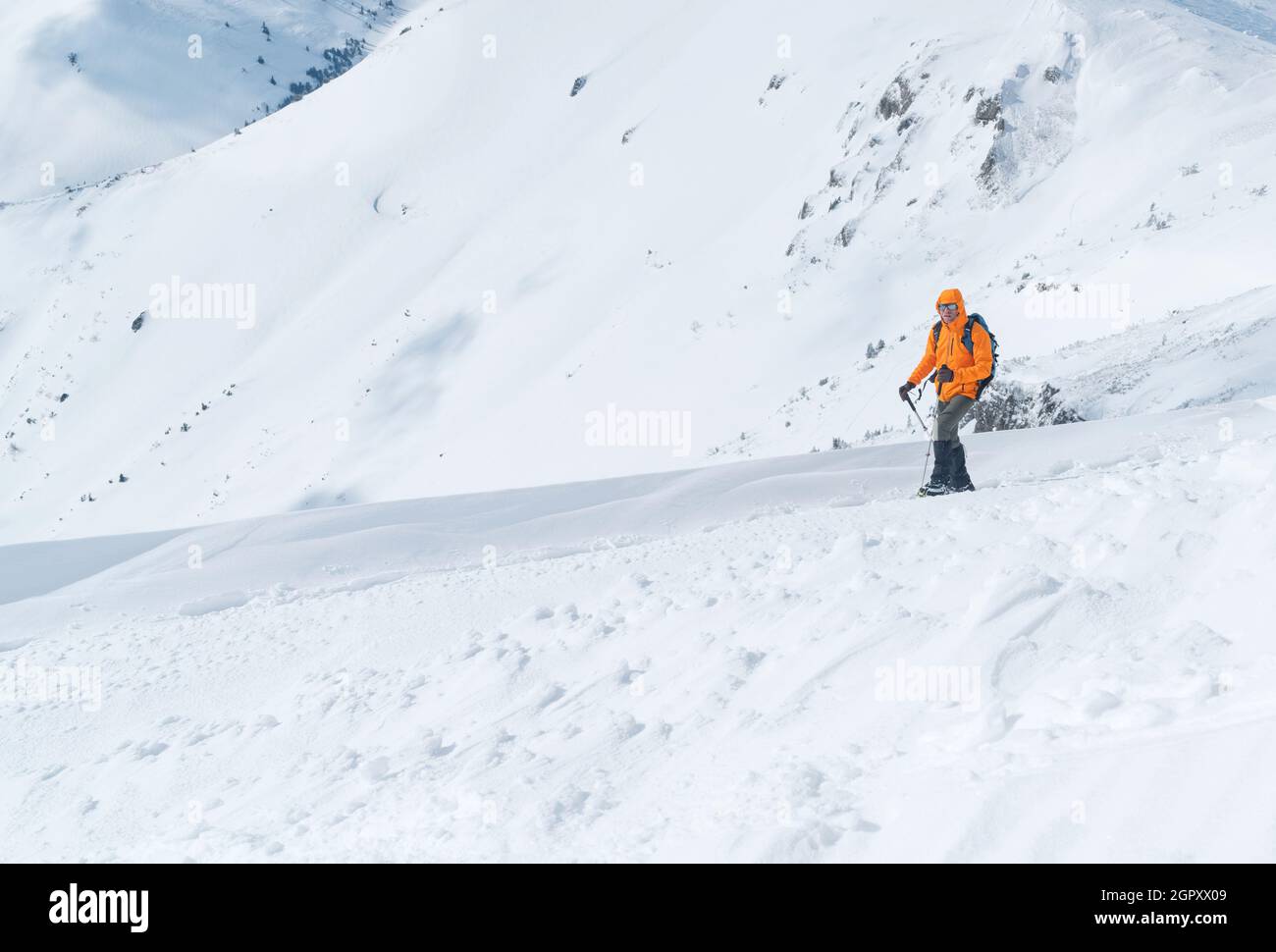 Hochbergsteiger bekleidete eine leuchtend orangefarbene Softshelljacke mit Trekkingstöcken, die den verschneiten Berggipfel erklimmen. Konzept für aktive Menschen auf Vel Stockfoto