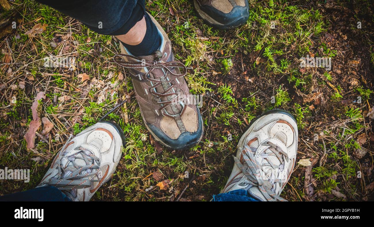 Wander- oder Wanderschuhe von zwei Reisenden, die im Wald stehen. Direkt über der Ansicht. Stockfoto