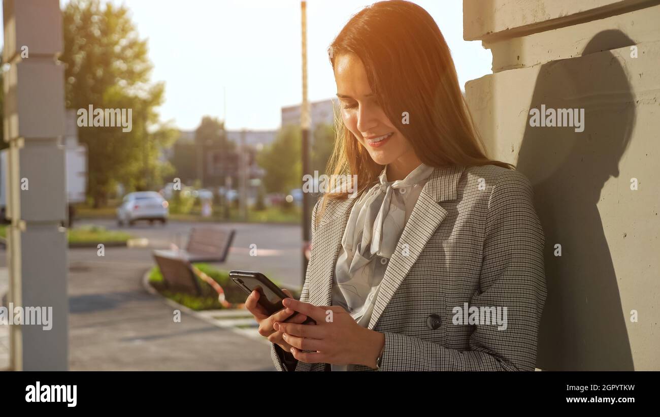 Junge Frau in einem Geschäftsanzug mit Telefon steht auf der Straße Stockfoto