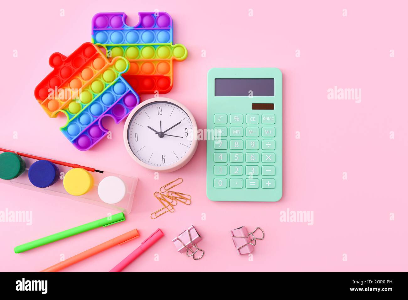 Flaches Lay von Schreibwaren, Uhr und Silikon-Spielzeug popit auf rosa Hintergrund Stockfoto