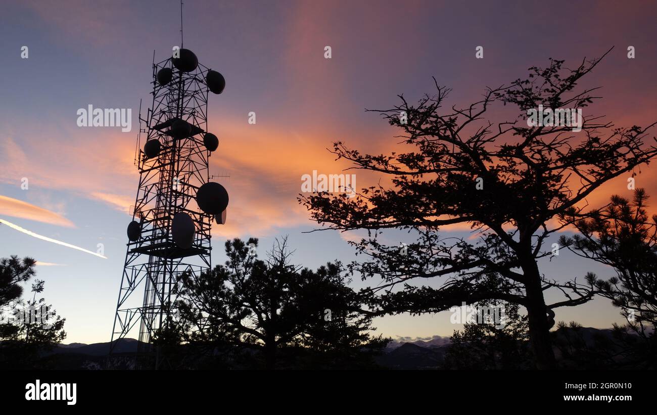 Gegenlicht-Fotografie mit der Silhouette von Bäumen und einer hohen Antenne mit orangefarbenem und blauem Hintergrund Stockfoto