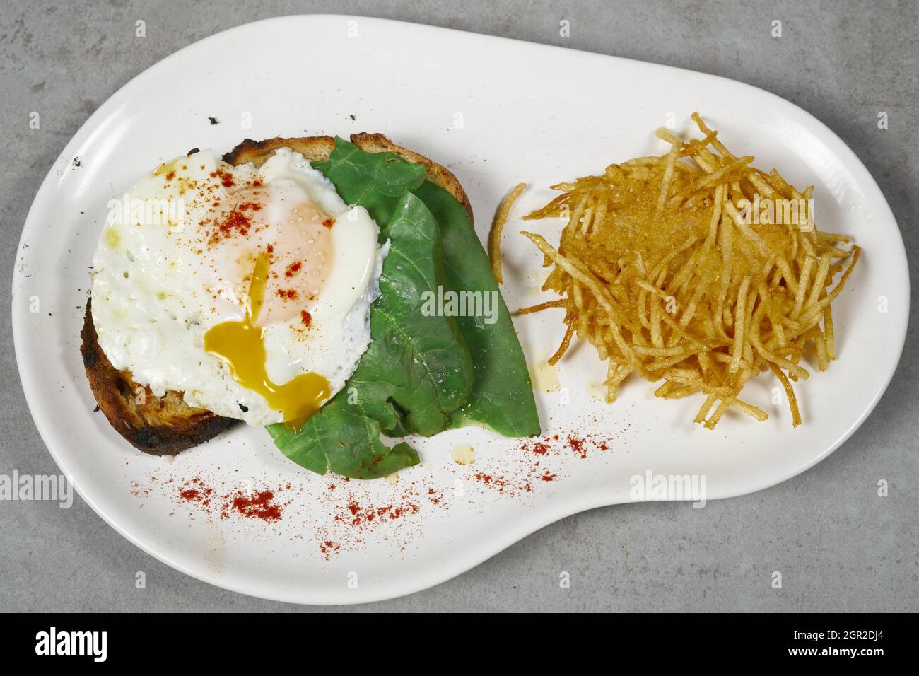 Blick von oben auf ein Frühstück mit pochiertem Ei und Kartoffelpastete auf einem abstrakten weißen Teller Stockfoto