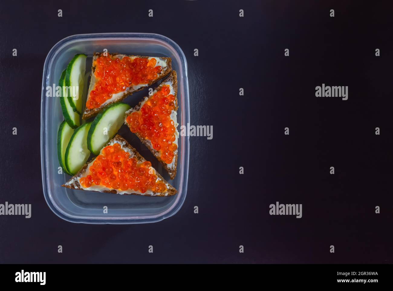 Neujahrsessen in einer transparenten Schachtel mit roten Kaviar-Sandwiches und frischen Gurken auf schwarzem Hintergrund. Hochwertige Fotos Stockfoto
