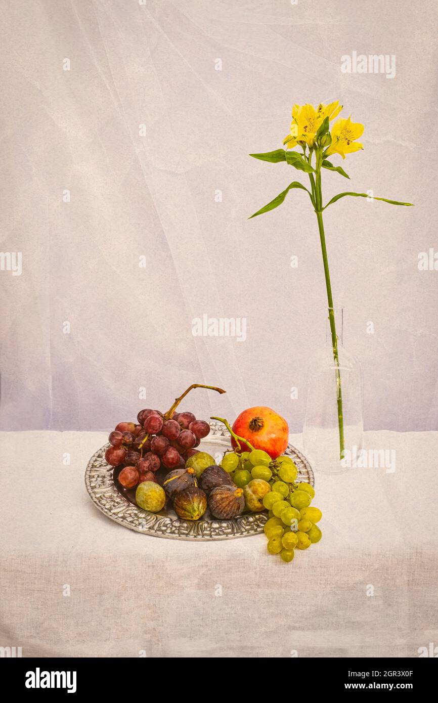 Stillleben von Blumen und Früchten auf einem erdfarbenen Hintergrund, mit Trauben, Feigen, einem Granatapfel auf einer silbernen Platte und einer gelben Lilie, einem Glasgefäß, ver Stockfoto