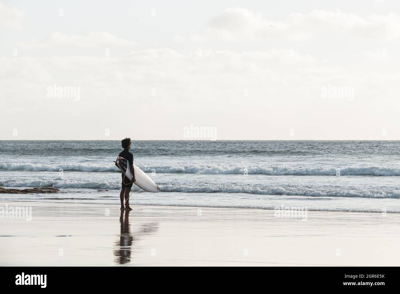 Surfer beobachten die Wellen, die bei Sonnenuntergang am Strand stehen Stockfoto