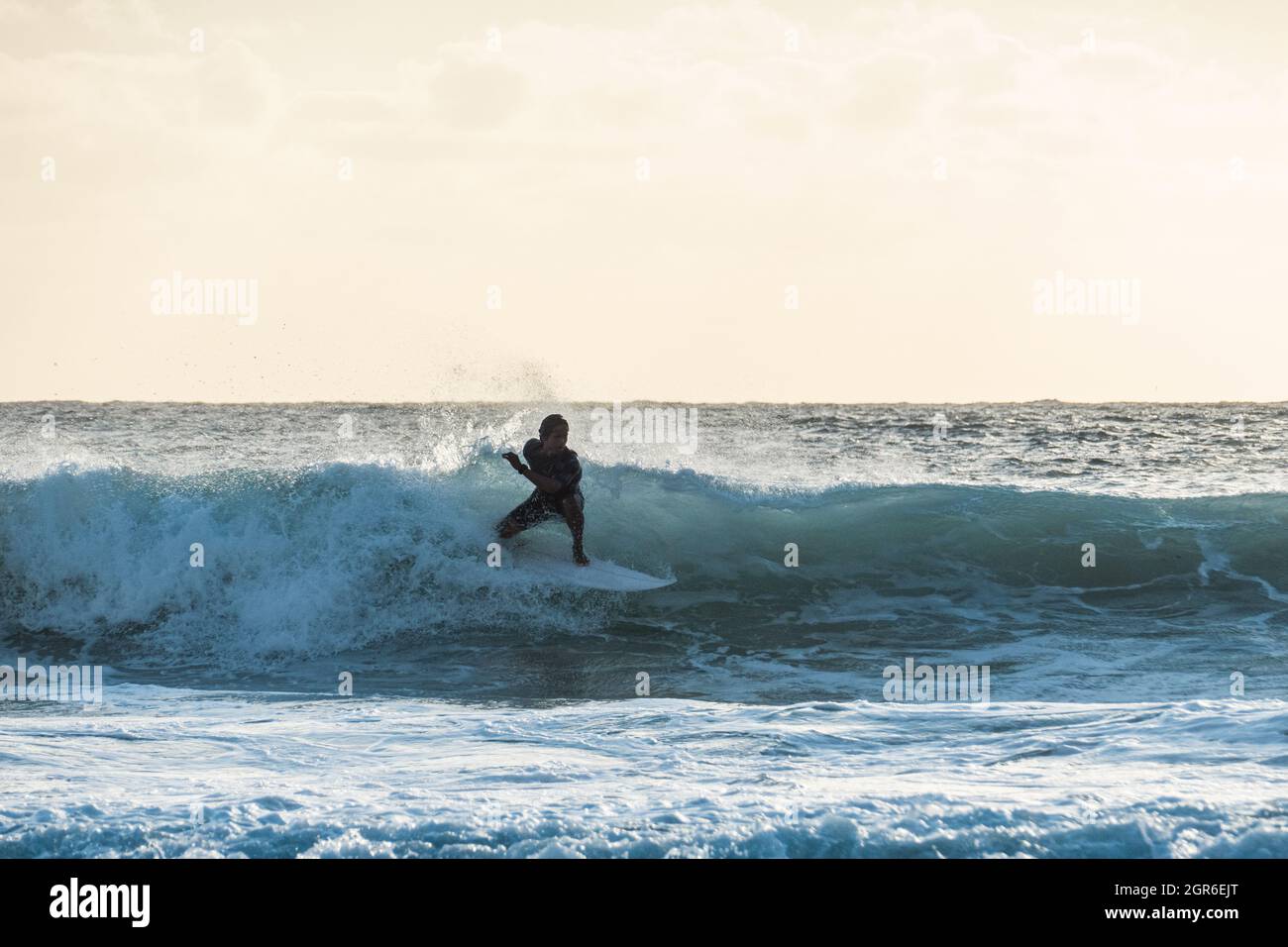 Junger Surfer, der bei Sonnenuntergang auf einer Welle reitet Stockfoto