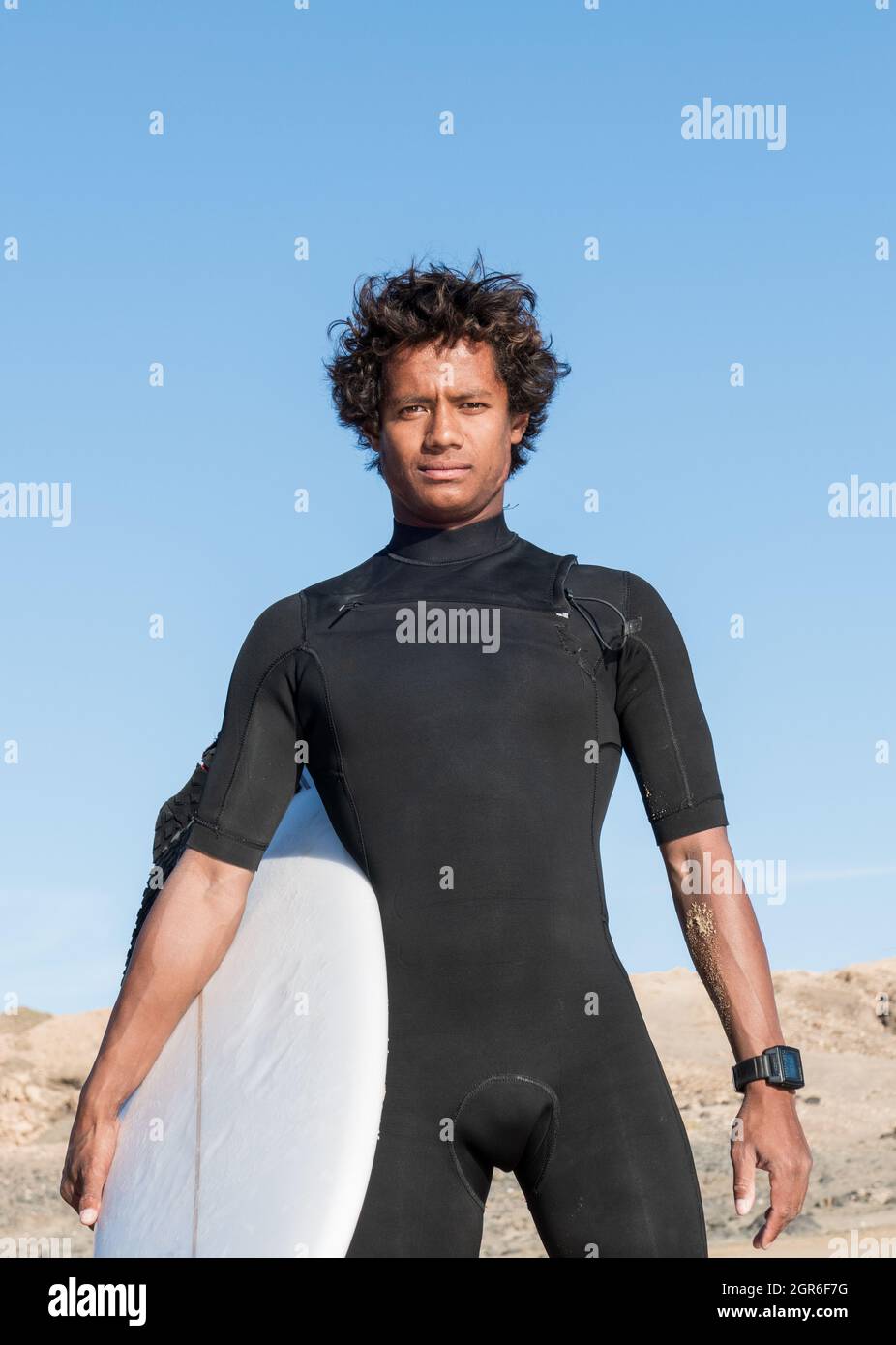 Junge afrikanische madagassische sportliche Surferportrait mit Surfbrett in kurzem schwarzen Neoprenanzug Stockfoto