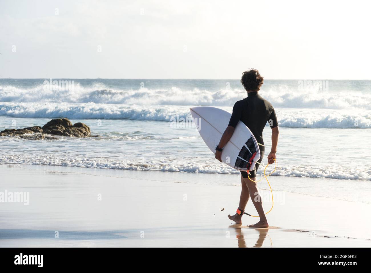 Nicht erkennbarer junger Surfer mit Shortboard, der am Strand entlang läuft und die Wellen beobachtet Stockfoto