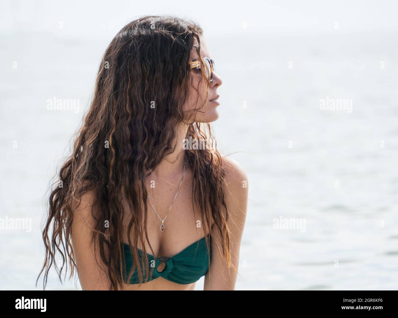 Attraktive junge hispanische Frau mit Bikini und Sonnenbrille am Strand Stockfoto