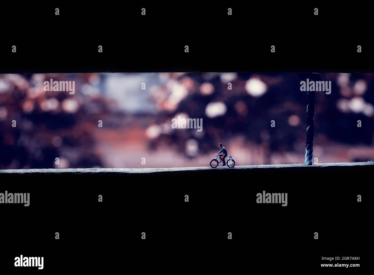 Miniaturfigur eines Mannes, der alleine mit dem Fahrrad unterwegs ist, in einem filmischen Ton am Nachmittag Stockfoto