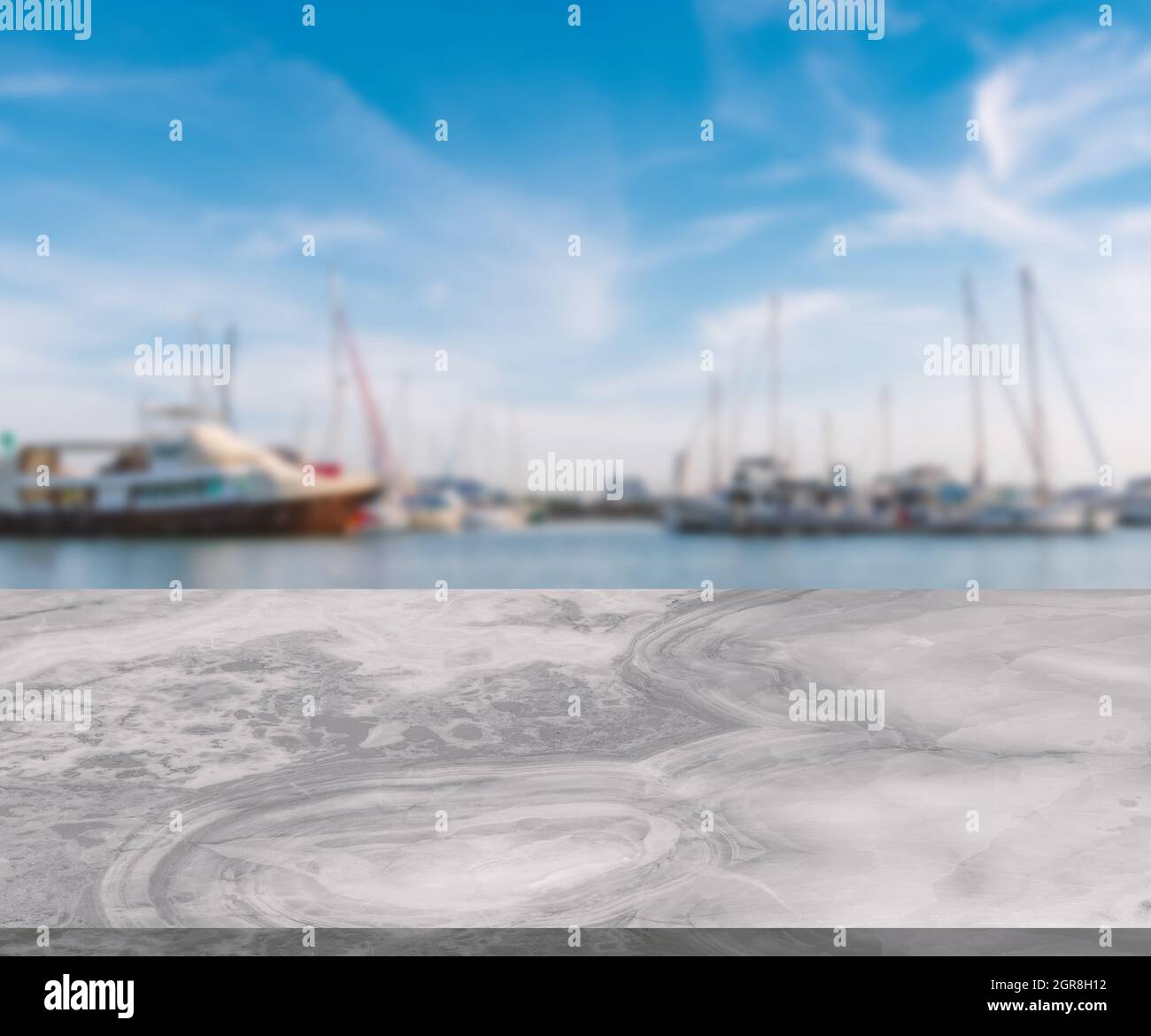 Weißer Marmortisch mit grauem Naturmuster, wenig glänzende Oberfläche, perspektivische Ansicht, verschwommener Hintergrund der Meeresbucht mit Yachten, blauer Himmel, leere s Stockfoto